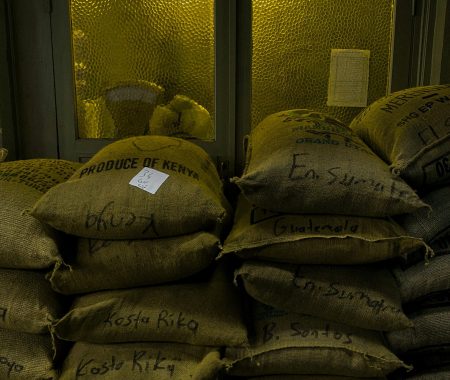 pexels-photo-26651061-26651061 Sacks of coffee beans labeled by country in a dimly lit warehouse setting.